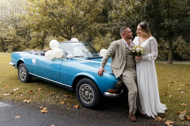 Couple de mariés posant devant une voiture décapotable bleue vintage