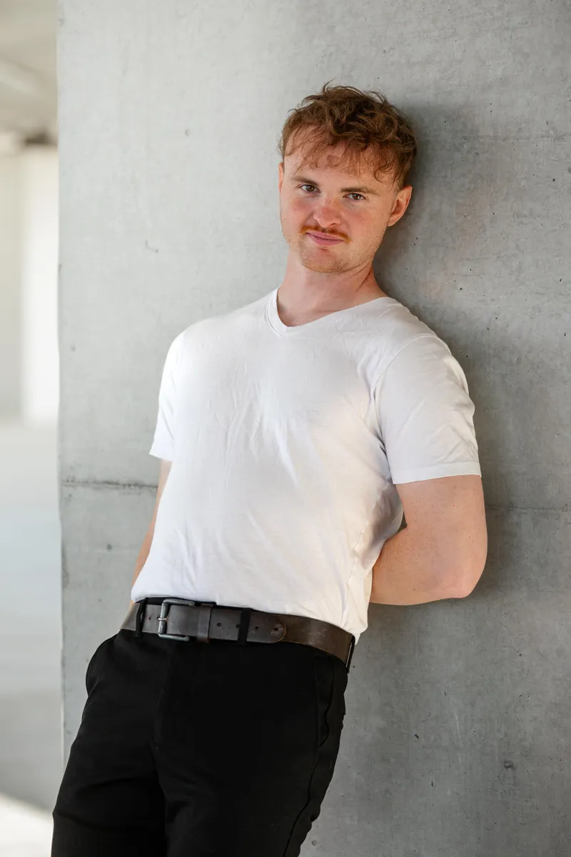 Portrait décontracté d'un comédien appuyé contre un mur en t-shirt blanc