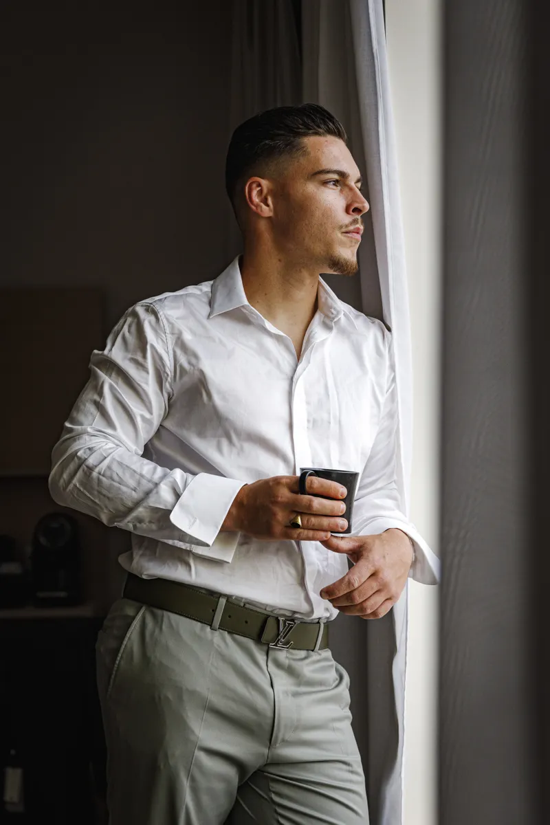 Marié en chemise blanche regardant par la fenêtre avant la cérémonie