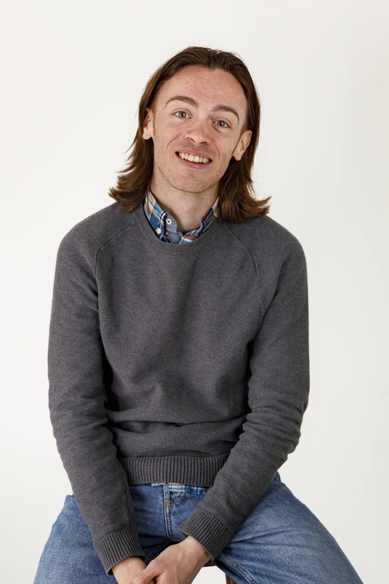 Portrait souriant d'un comédien en pull gris sur fond clair
