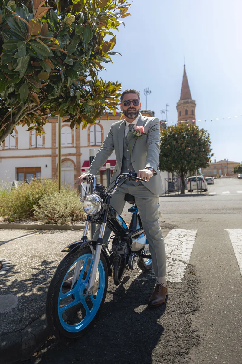 Marié en costume arrivant en mobylette devant une église