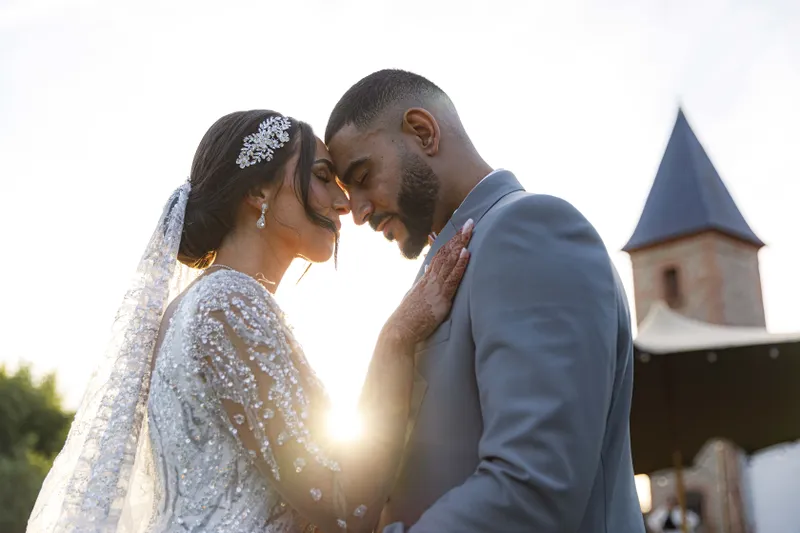 Couple de mariés front contre front au coucher du soleil devant un château