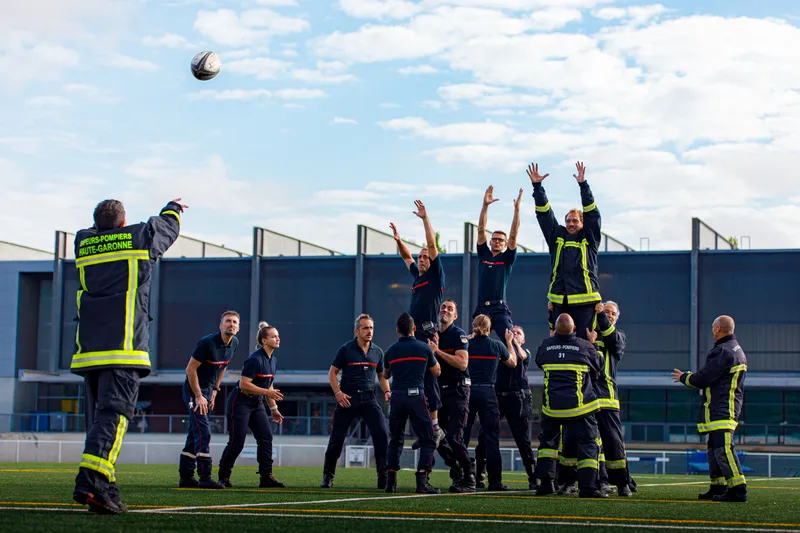 Pompiers en tenue d'intervention jouant au rugby sur un terrain synthétique
