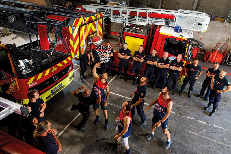 Pompiers jouant au basketball dans le garage de la caserne entre les camions