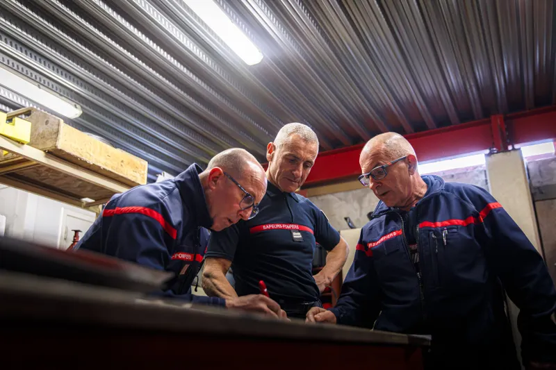 Trois sapeurs-pompiers vétérans inspectant un véhicule dans l'atelier