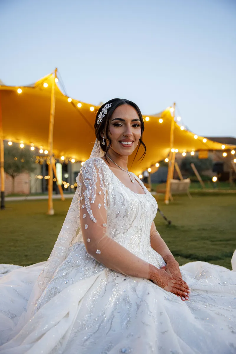 Portrait de la mariée souriante avec son voile devant une tente illuminée