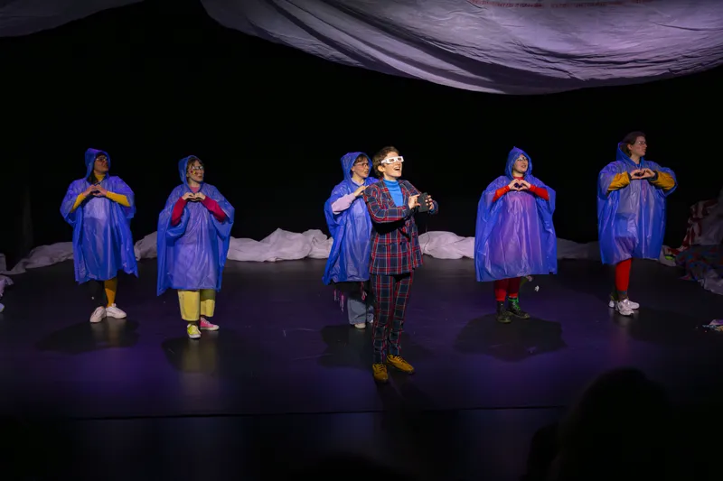 Troupe de comédiens en ponchos bleus jouant une scène de théâtre
