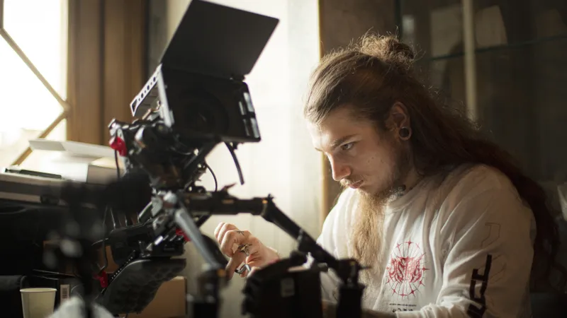 Cadreur aux cheveux longs concentré derrière sa caméra cinéma