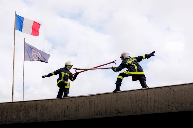Deux pompiers en tenue complète tirant une lance à incendie sur un toit