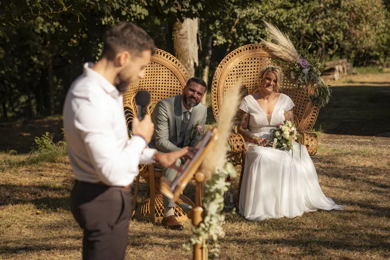 Cérémonie laïque de mariage en extérieur avec les mariés assis sur des fauteuils en rotin