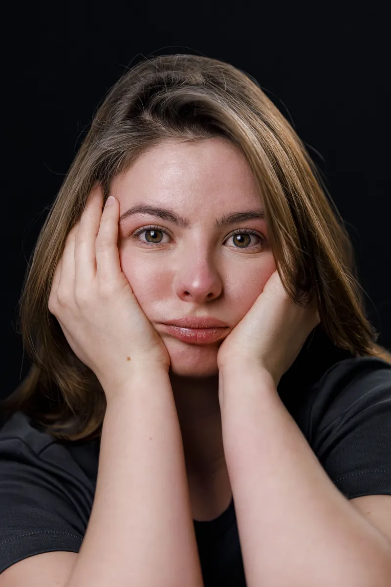 Portrait expressif d'une comédienne le visage dans les mains sur fond sombre