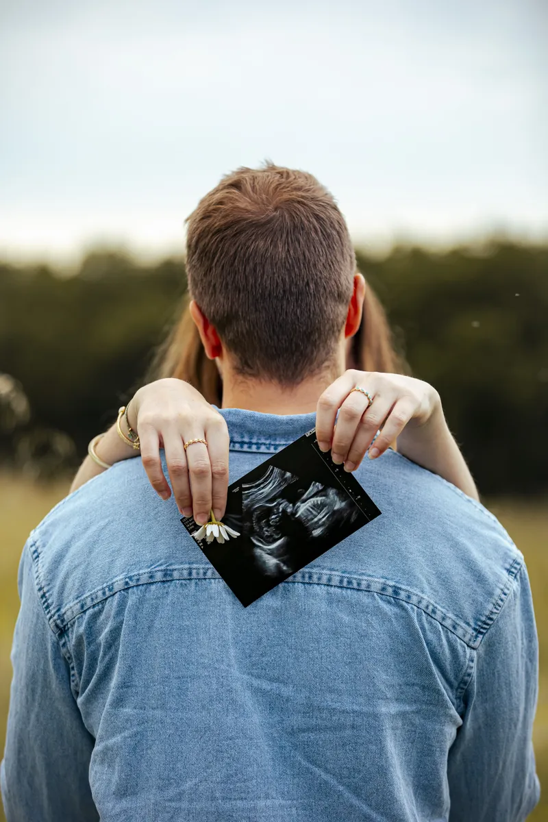 Couple enlacé montrant une échographie de bébé dans un champ au coucher du soleil