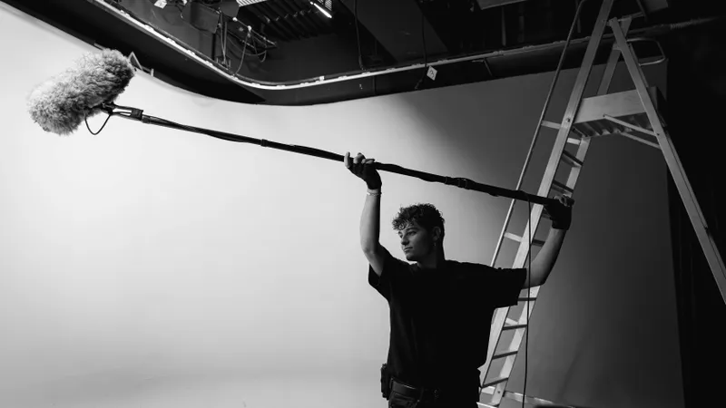 Perchiste en silhouette tenant une perche son en studio, photo noir et blanc