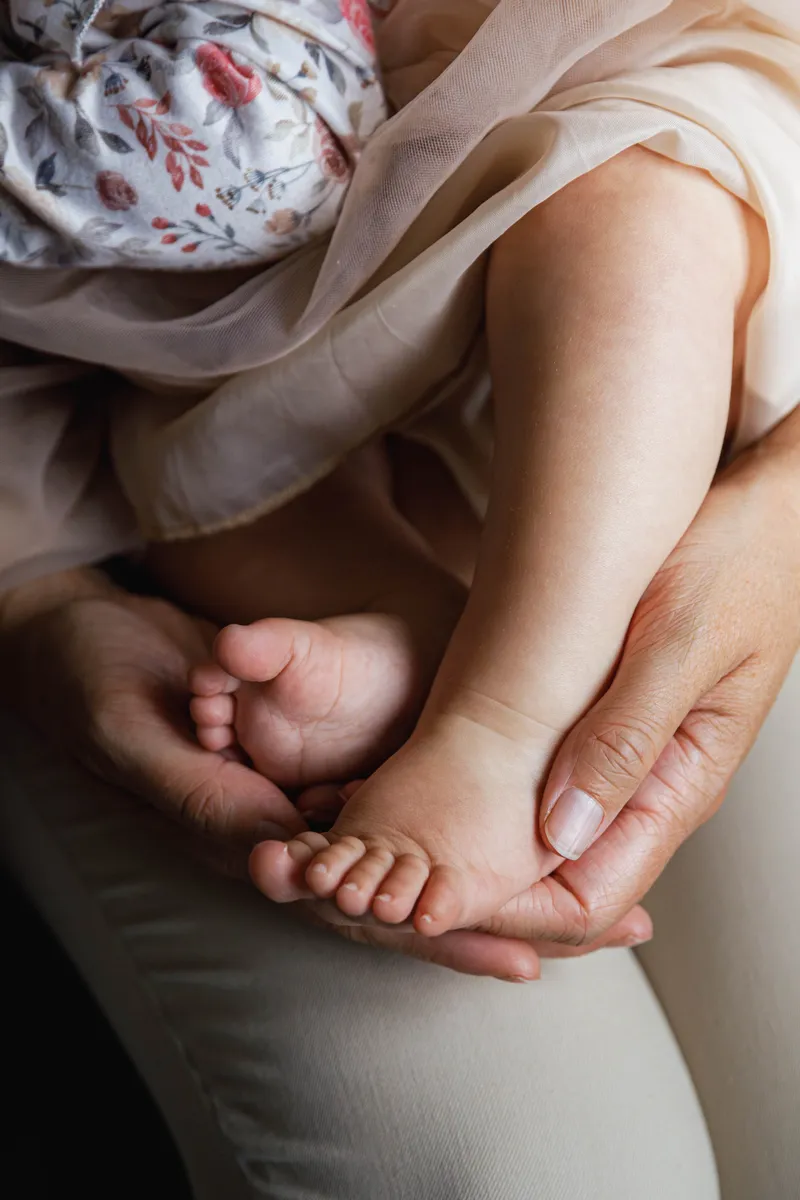 Gros plan sur les petits pieds d'un bébé tenus dans les mains de sa maman