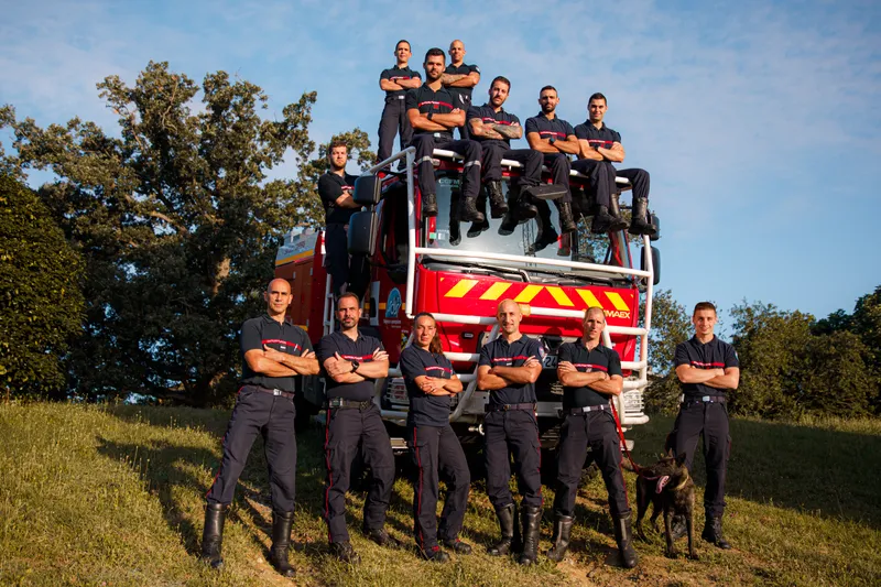 Groupe de pompiers posant avec un chien devant un camion en pleine nature