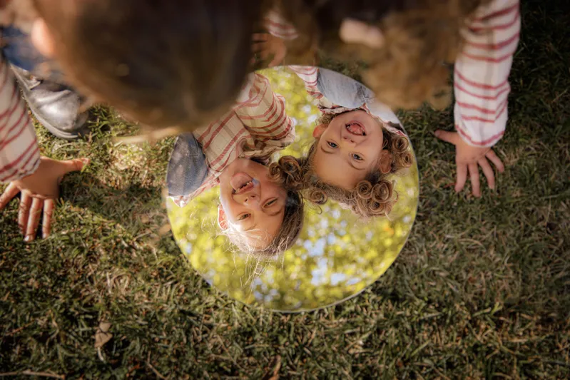 Deux soeurs se regardant dans un miroir rond posé dans l'herbe