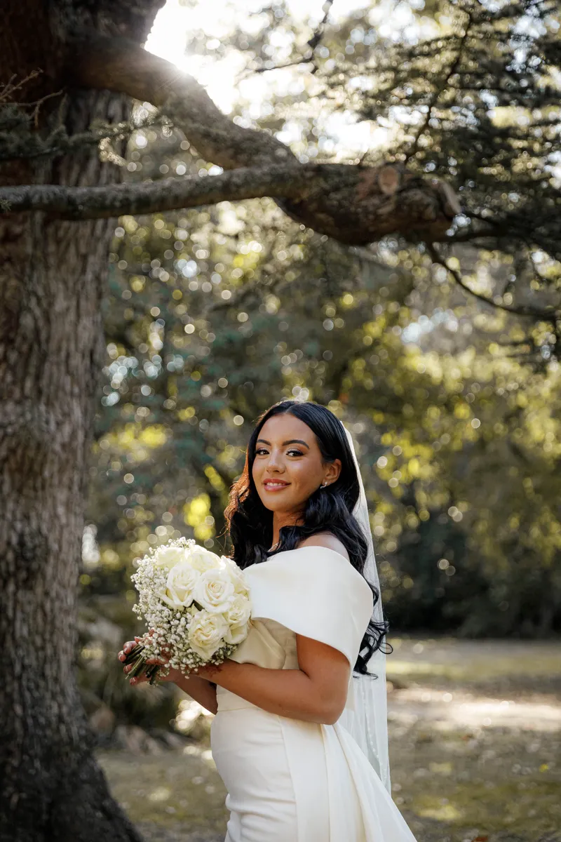 Mariée souriante avec son bouquet de roses blanches sous un arbre