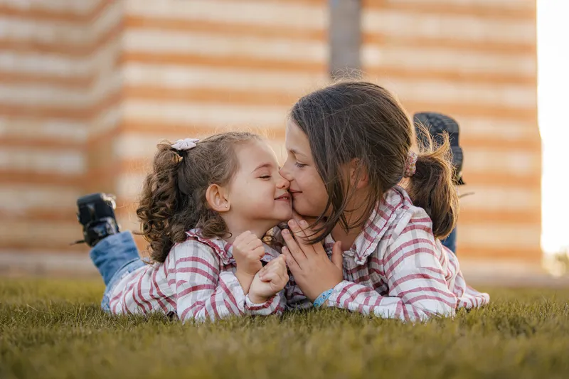 Petite fille embrassant sa grande soeur allongées dans l'herbe