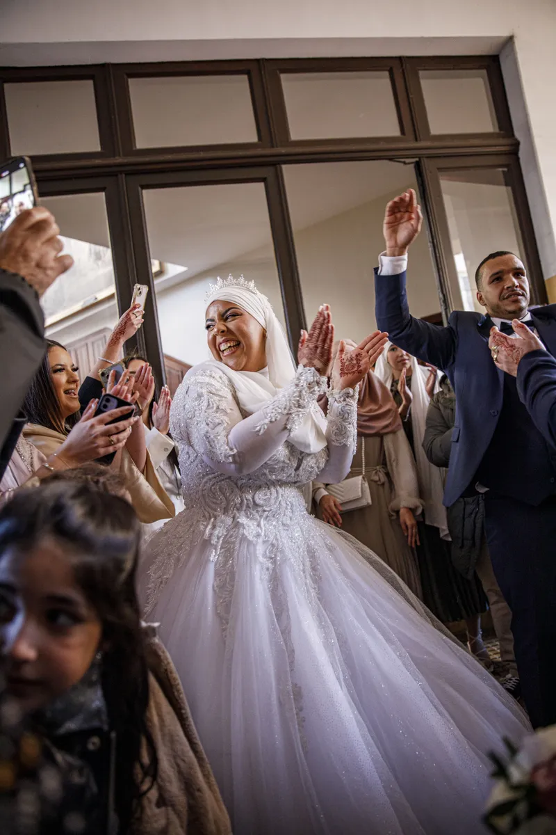 Mariée en hijab et robe blanche accueillie par les applaudissements des invitées