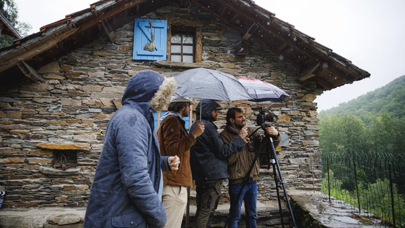 Équipe de tournage filmant sous la pluie devant une maison en pierre