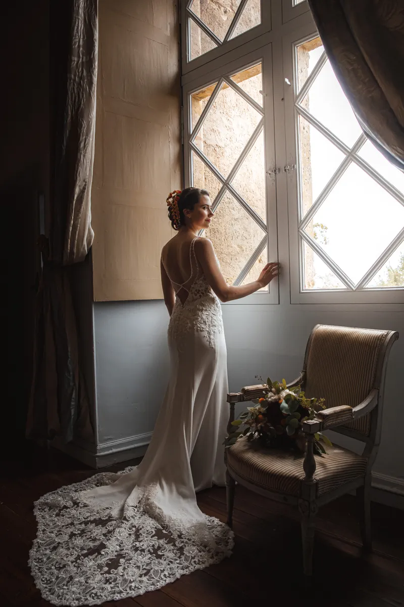 Mariée en robe de dentelle posant devant une fenêtre à croisillons