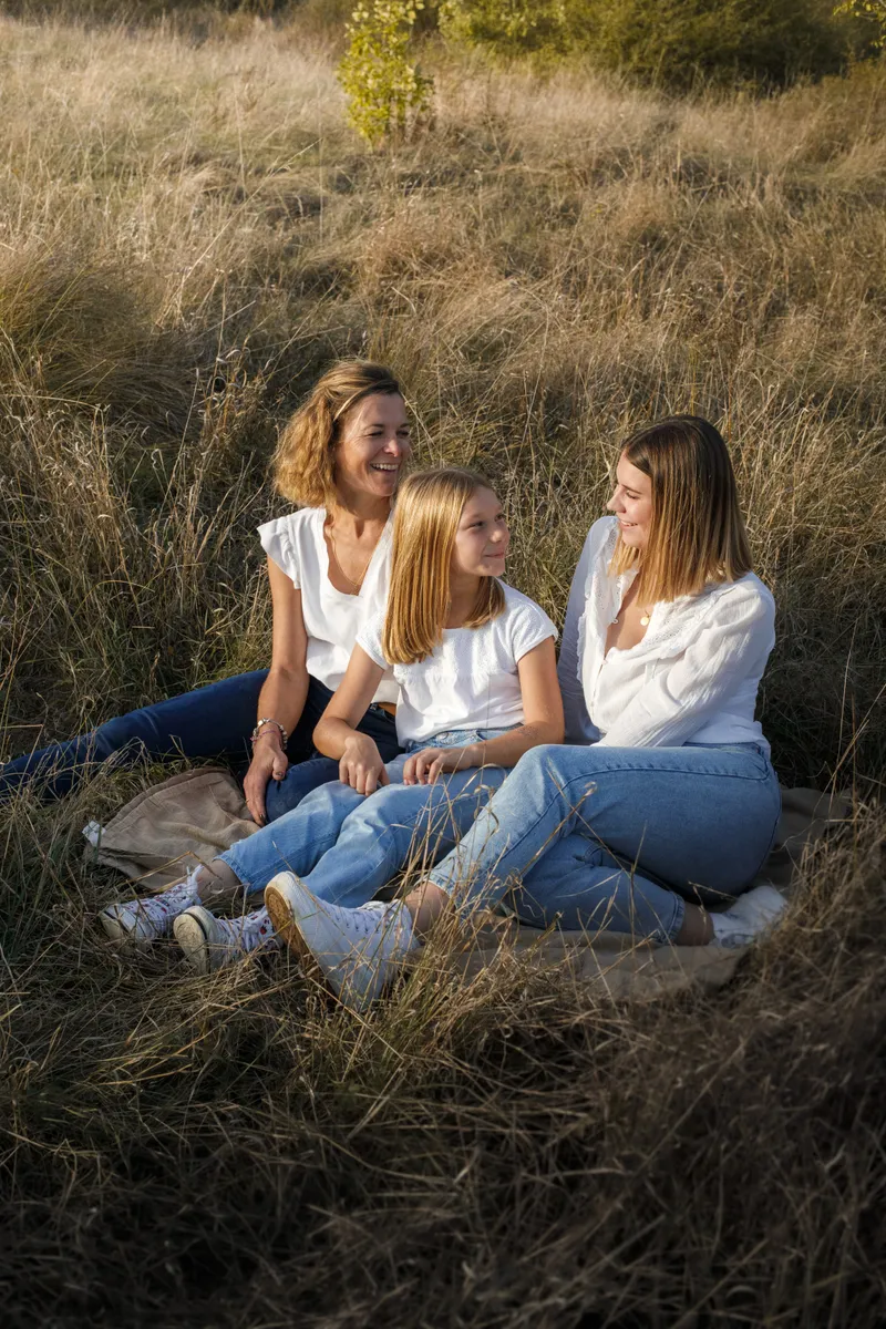 Mère et ses deux filles assises dans un champ doré au coucher du soleil