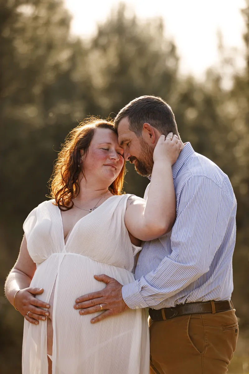 Couple de futurs parents enlacés tendrement au coucher du soleil