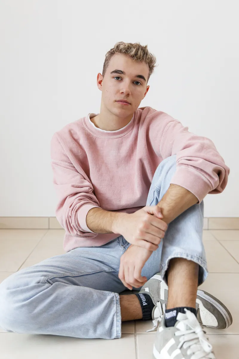 Portrait d'un jeune comédien assis au sol en sweat rose