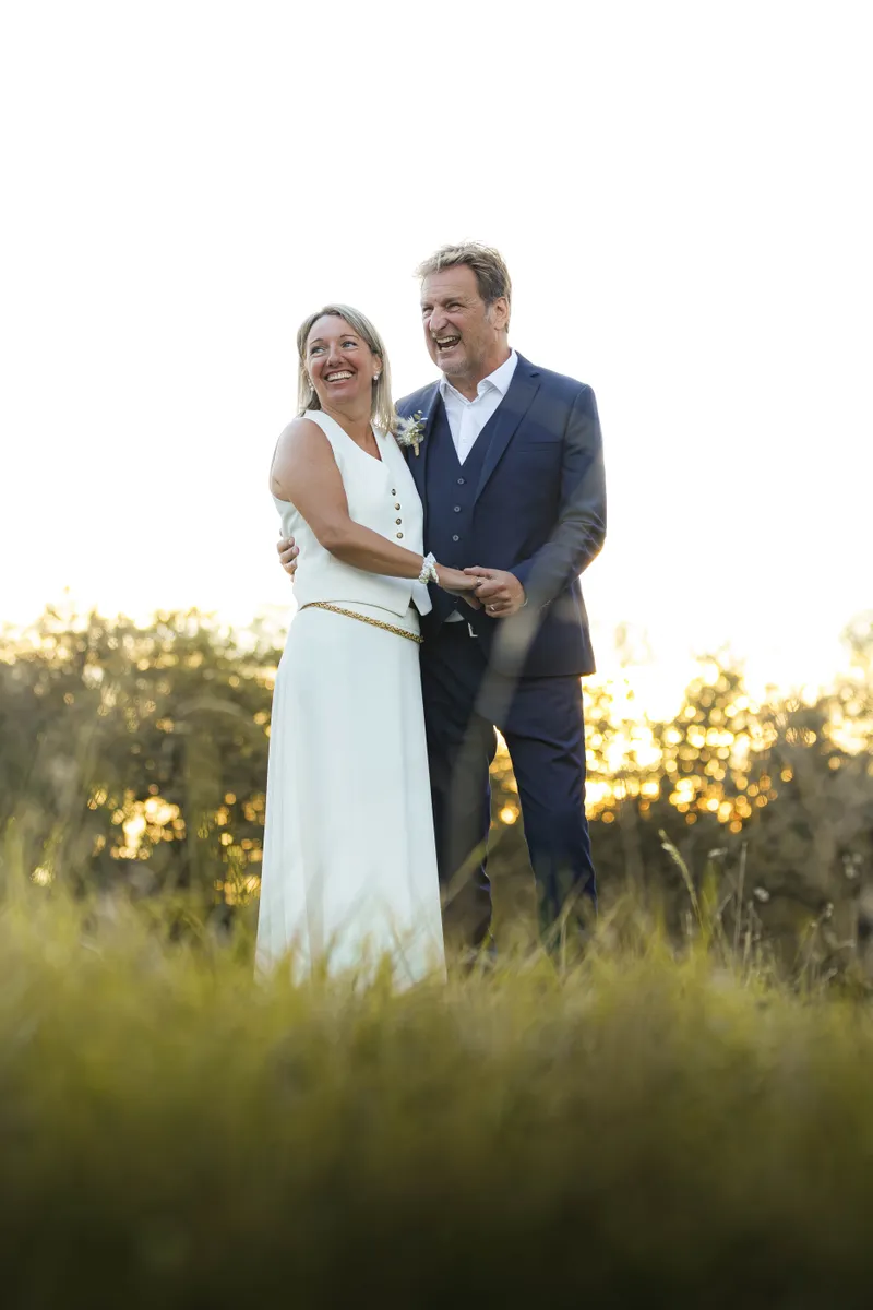 Couple de mariés posant ensemble dans un champ au coucher du soleil