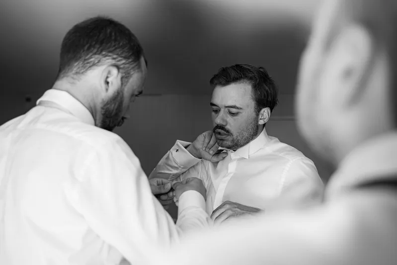 Témoins aidant le marié à ajuster sa chemise, photo en noir et blanc