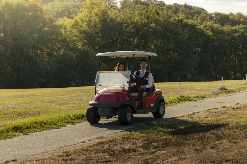 Couple de mariés arrivant en voiturette de golf à leur réception en pleine nature