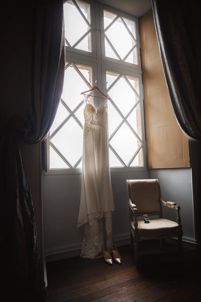 Robe de mariée suspendue devant une fenêtre à croisillons dans un château