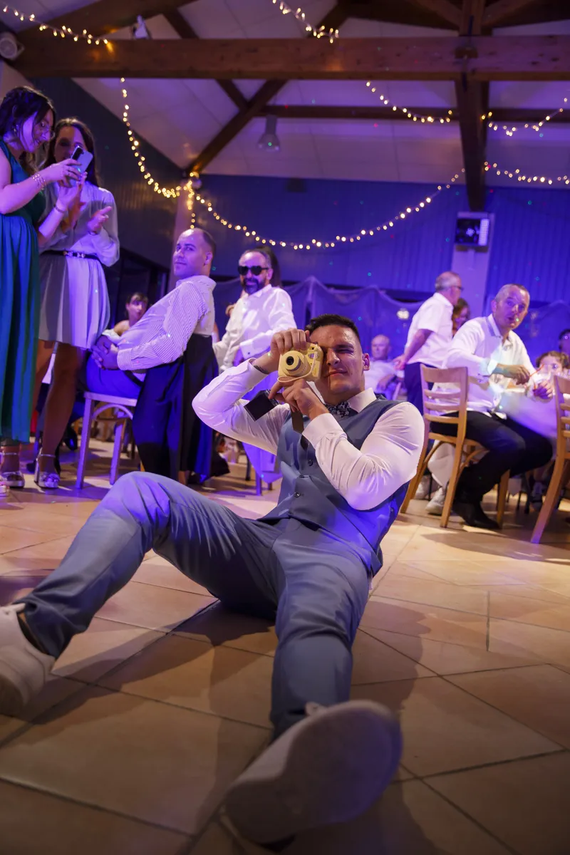 Invité assis au sol prenant une photo avec un appareil doré lors de la soirée