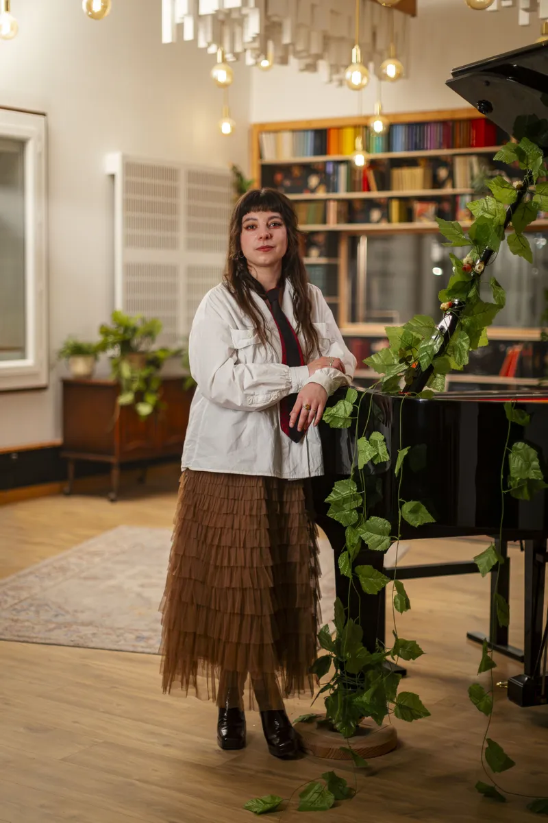 Portrait d'une musicienne debout près d'un piano à queue décoré de lierre