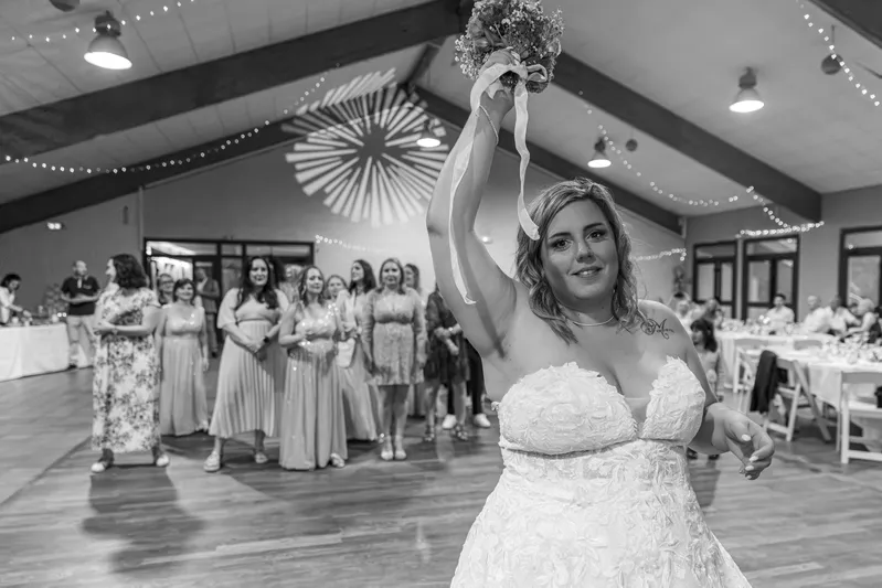 Mariée lançant son bouquet devant les invitées en noir et blanc