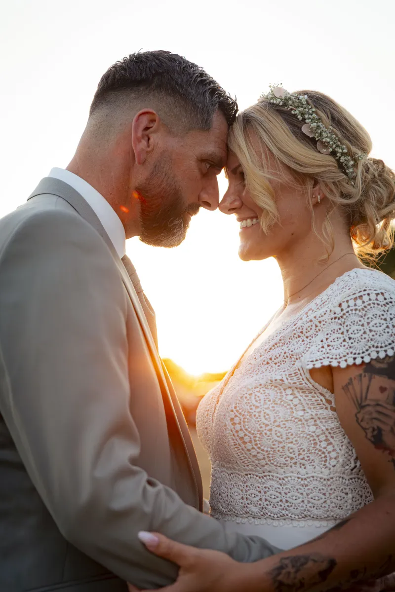 Couple de mariés front contre front au coucher du soleil avec couronne de fleurs