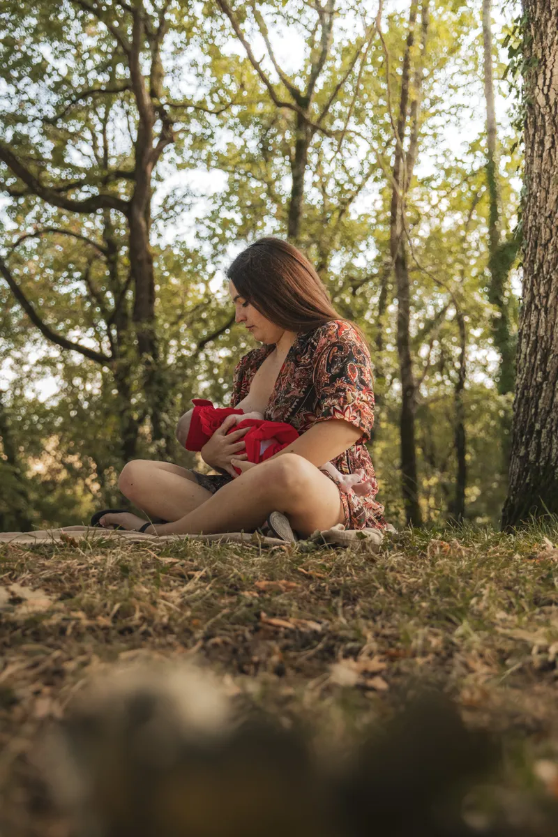 Maman allaitant son bébé assise au pied d'un arbre en forêt