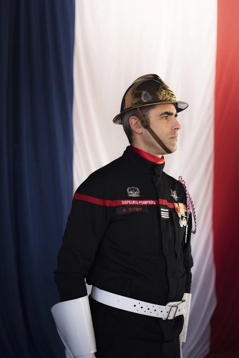 Portrait d'un sapeur-pompier en tenue de cérémonie devant le drapeau tricolore