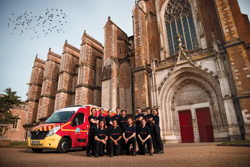 Équipe de pompiers posant devant une cathédrale en briques avec un véhicule de secours