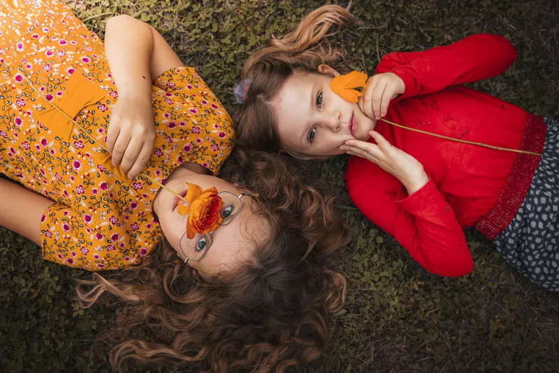 Deux petites filles allongées dans l'herbe tenant des feuilles d'automne